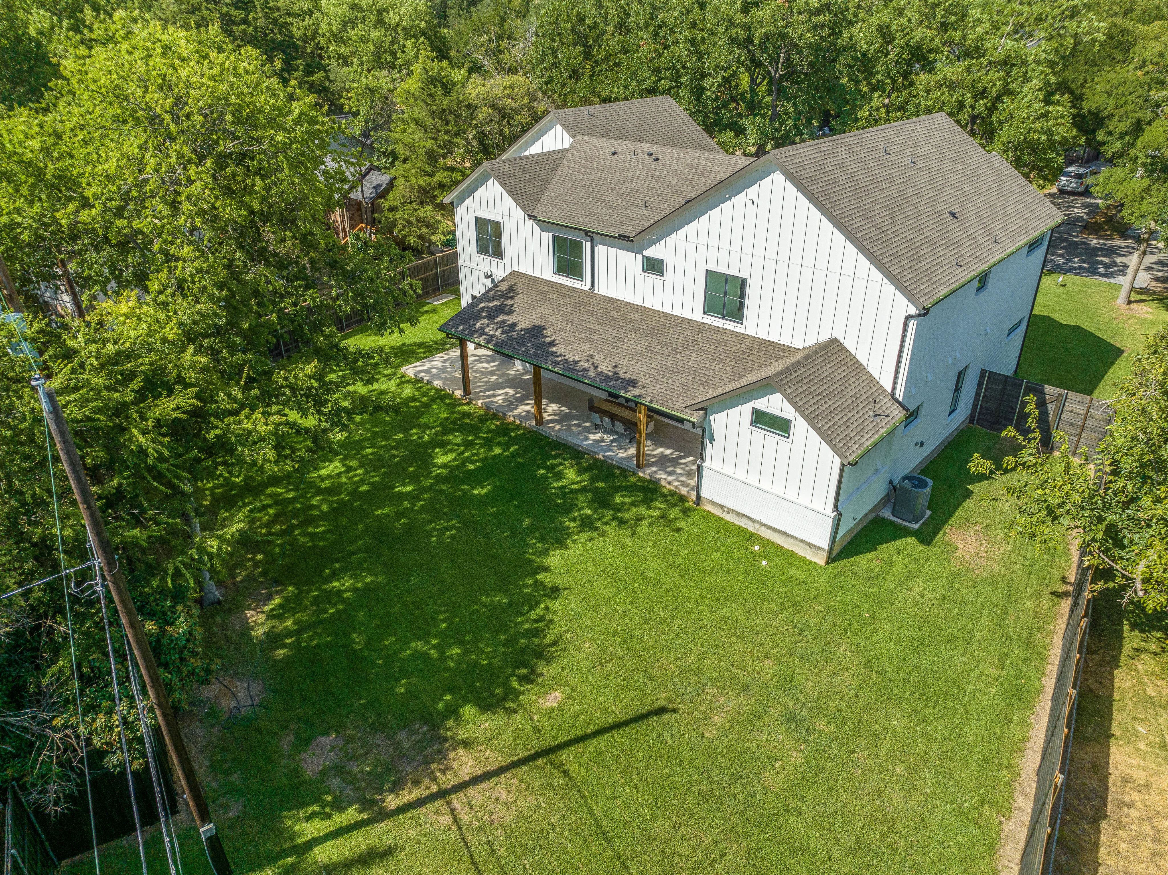 Elevated rear view showing the residence, covered porch, rooflines, lawn, and surrounding tree canopy