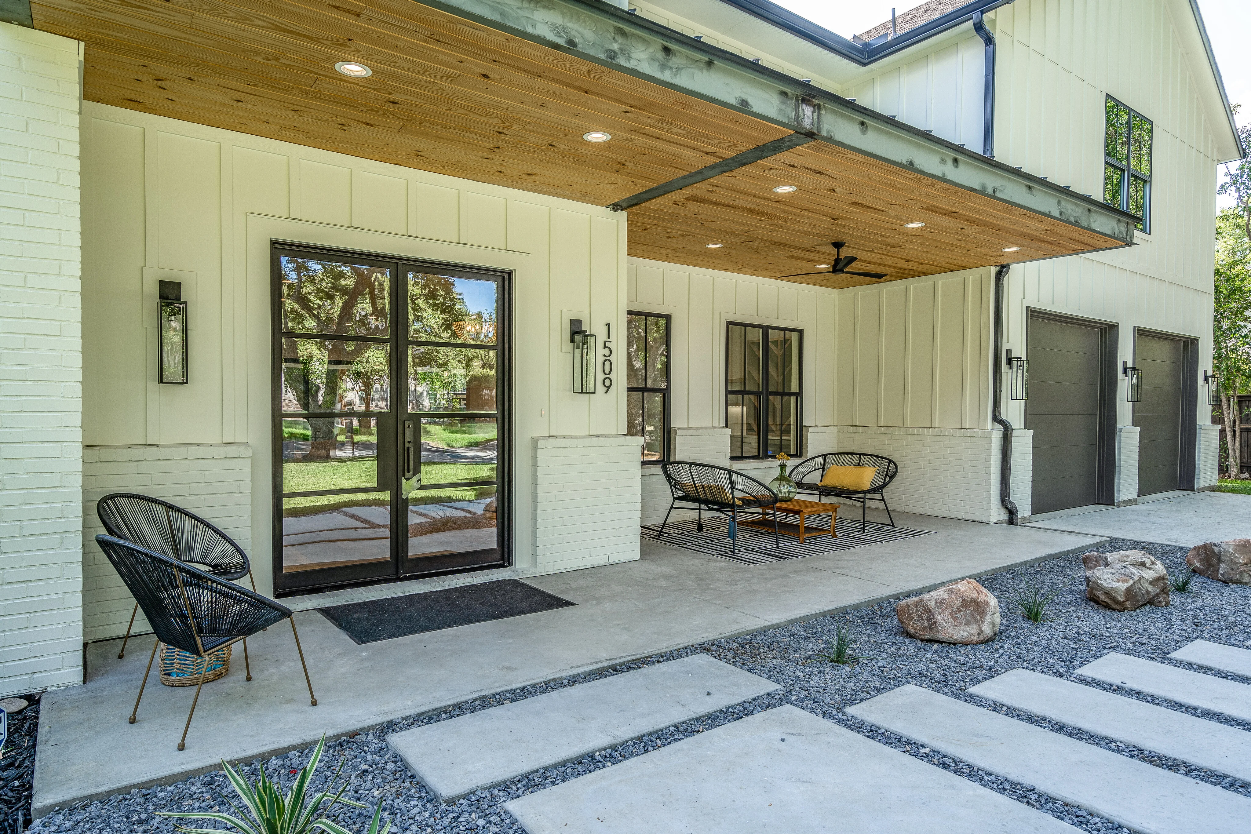 Covered porch with a warm wood ceiling, black-framed glass doors, seating, and garage access
