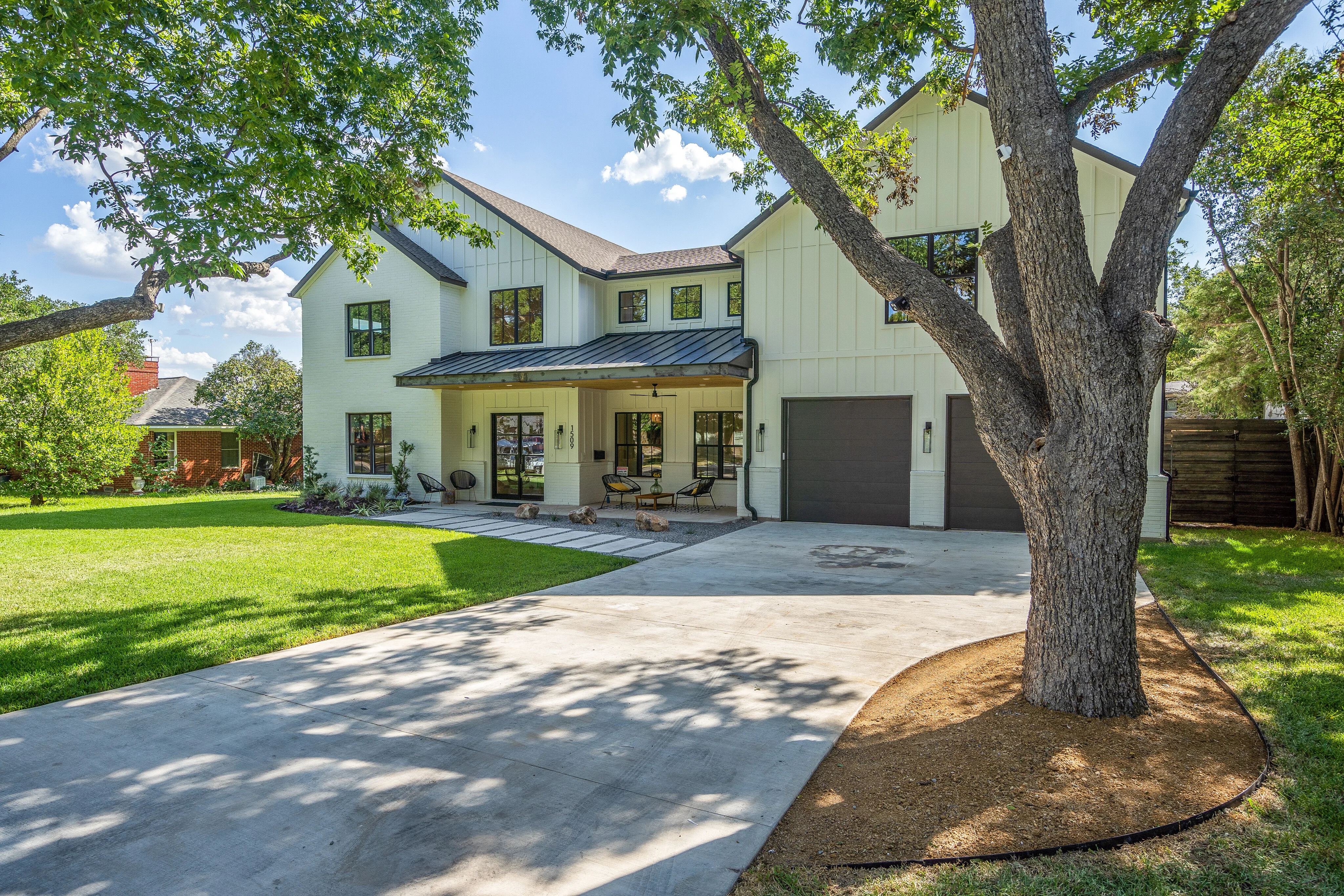 Front elevation of 1509 El Campo Drive with white brick, board-and-batten siding, black-framed windows, and mature trees