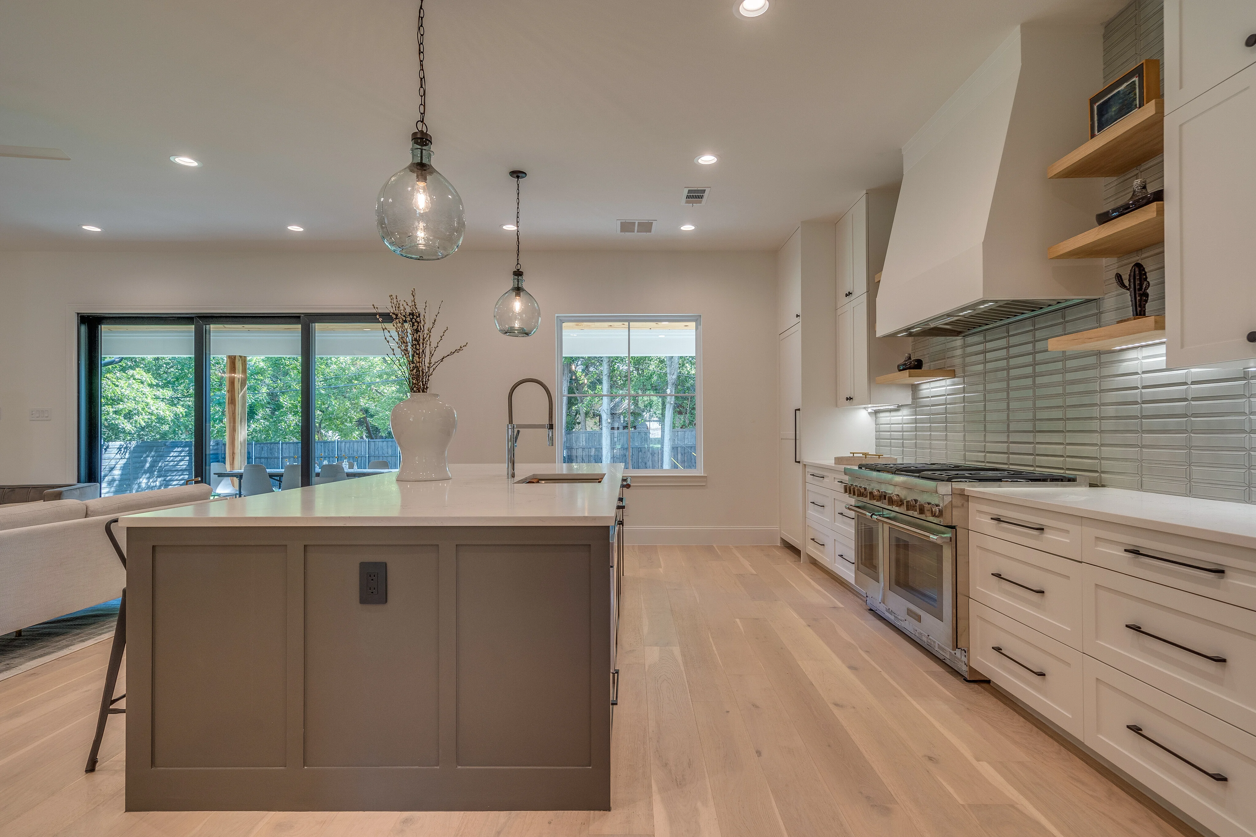 Wide kitchen with a large island, white cabinetry, pendant lighting, and professional range