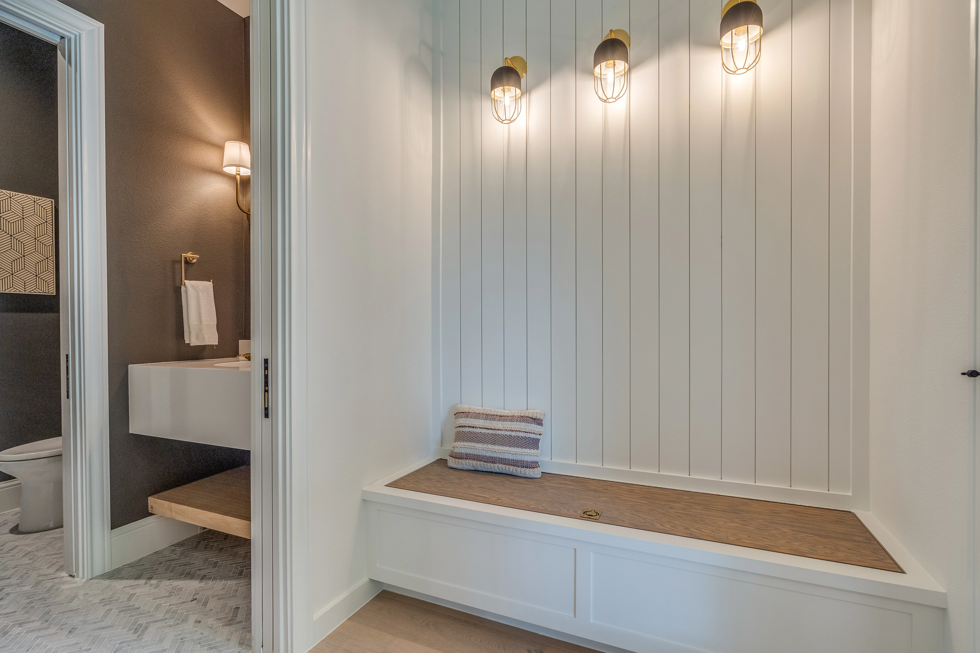 Mudroom bench with vertical paneling, wood seat, open cubbies, and wall lights