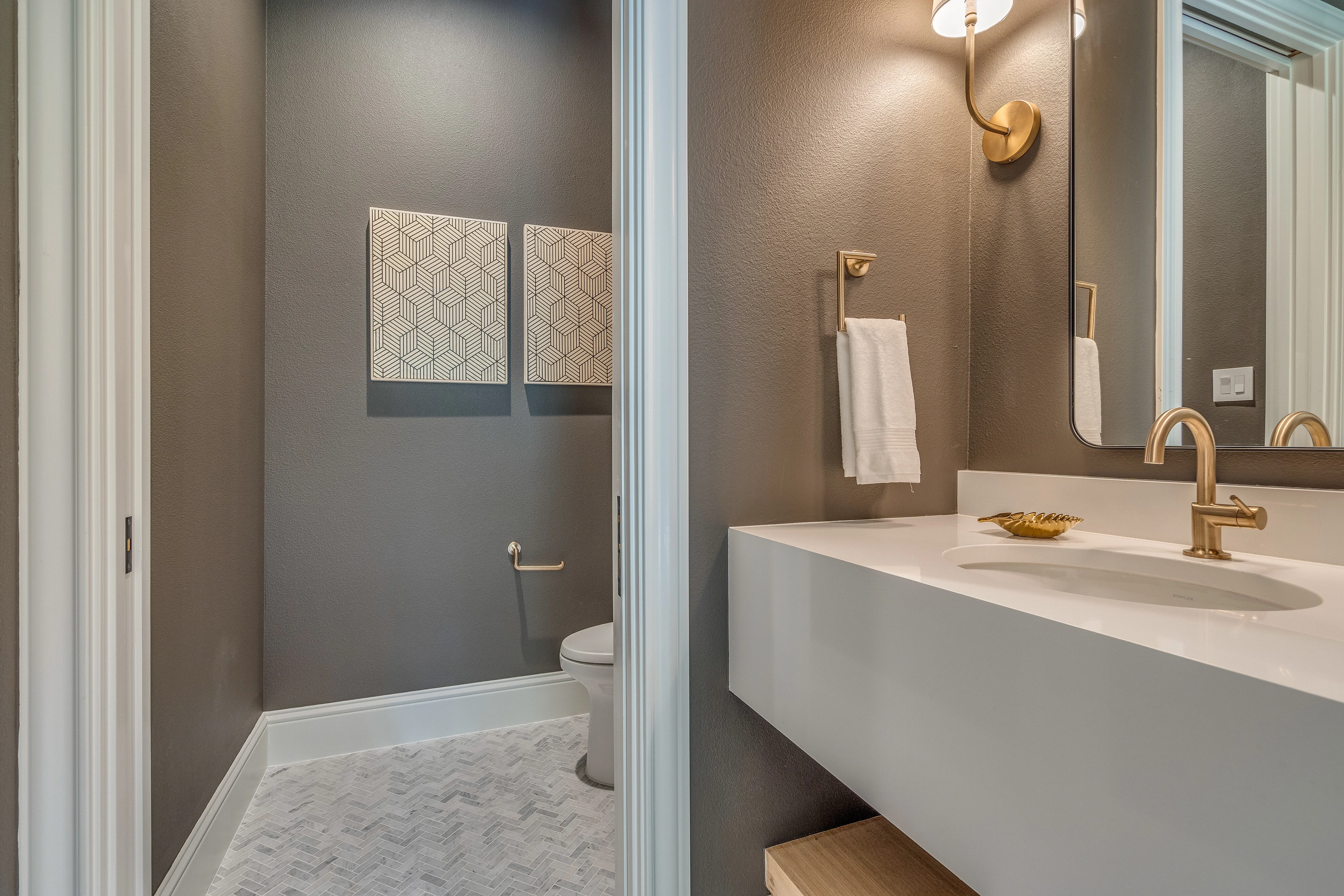 Powder room with warm gray walls, pale stone vanity, and brass fixtures
