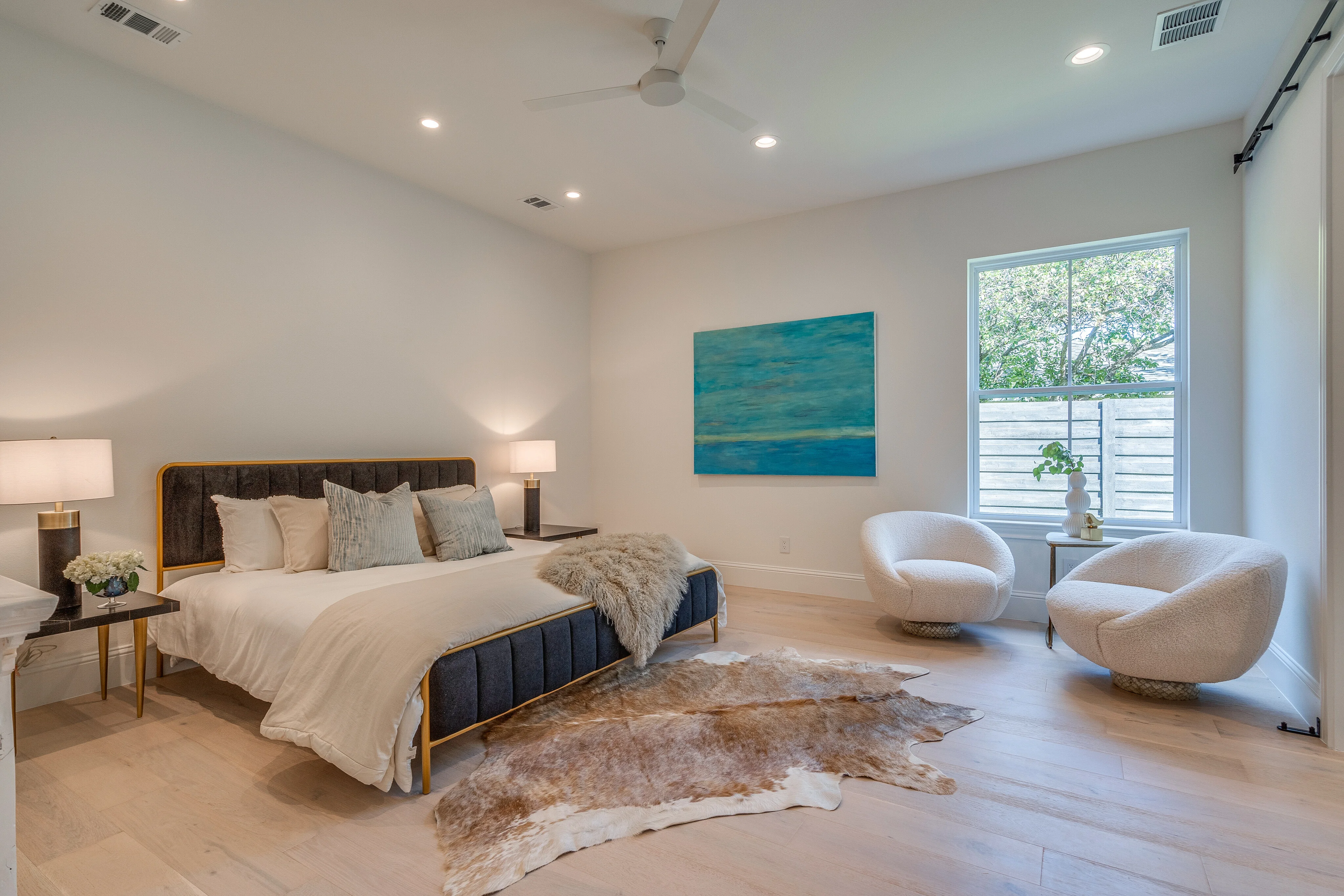 Bedroom suite with pale wood floors, sitting chairs, and an adjoining bathroom