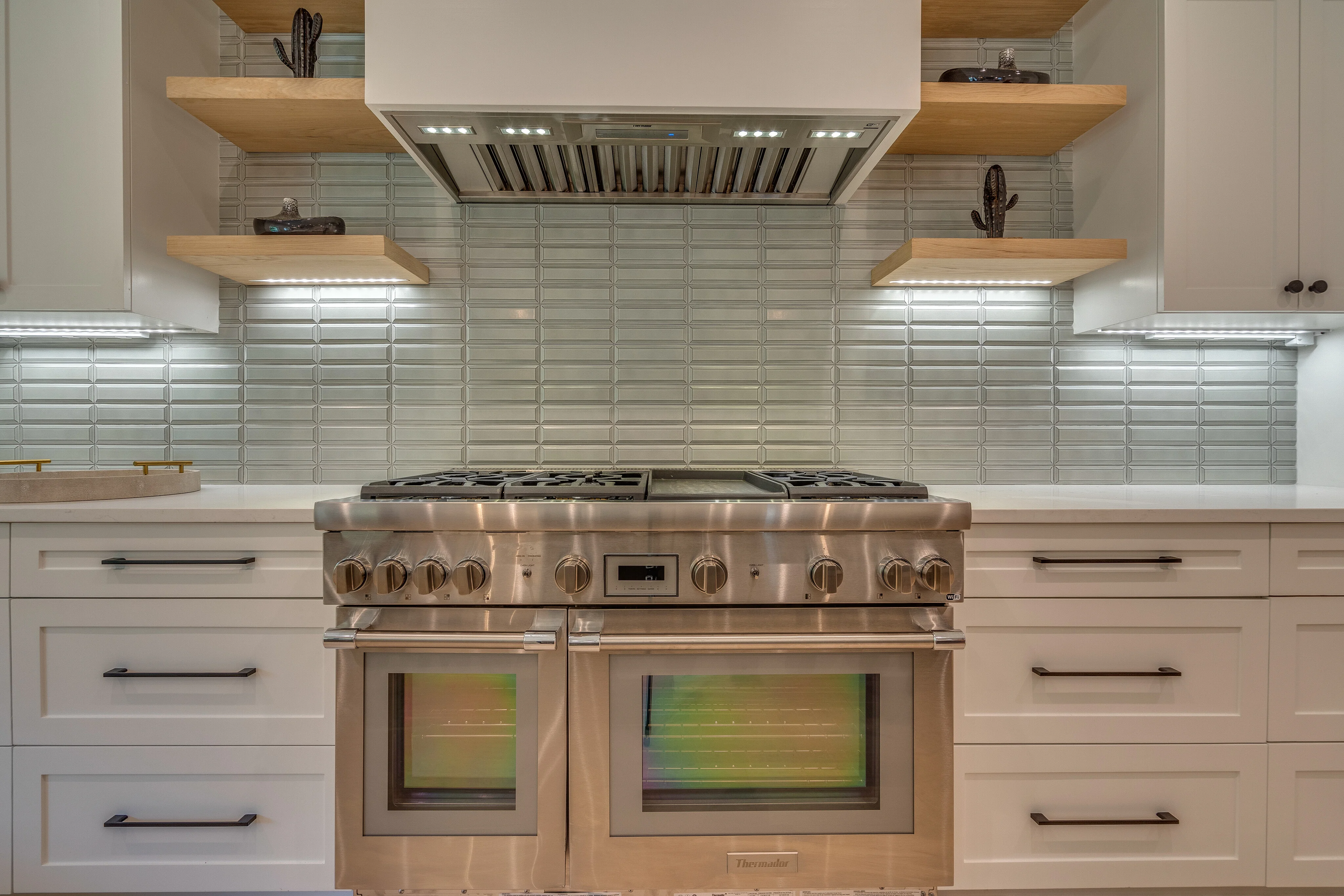 Professional stainless range beneath a custom hood with dimensional tile and wood shelving