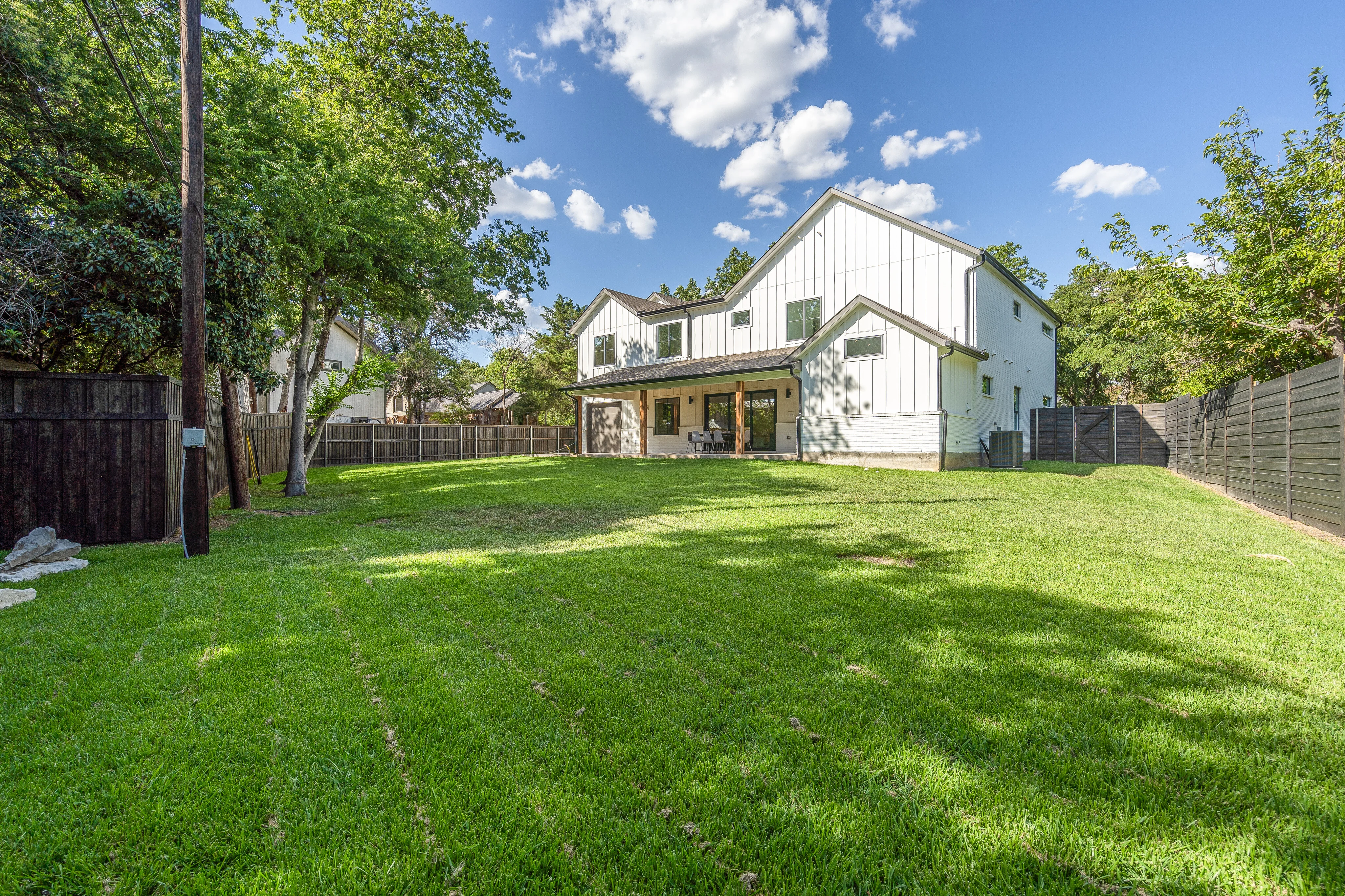 Rear elevation and broad lawn framed by mature trees and a privacy fence